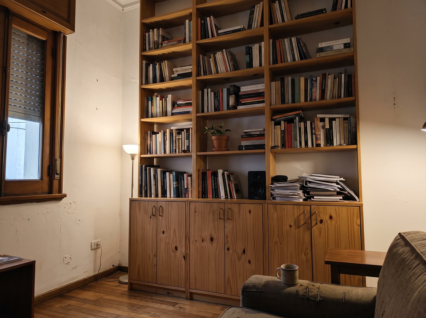 Biblioteca de pino macizo de piso a techo con estantes abiertos arriba y puertas cerradas abajo, llena de libros, en un living con techo alto.