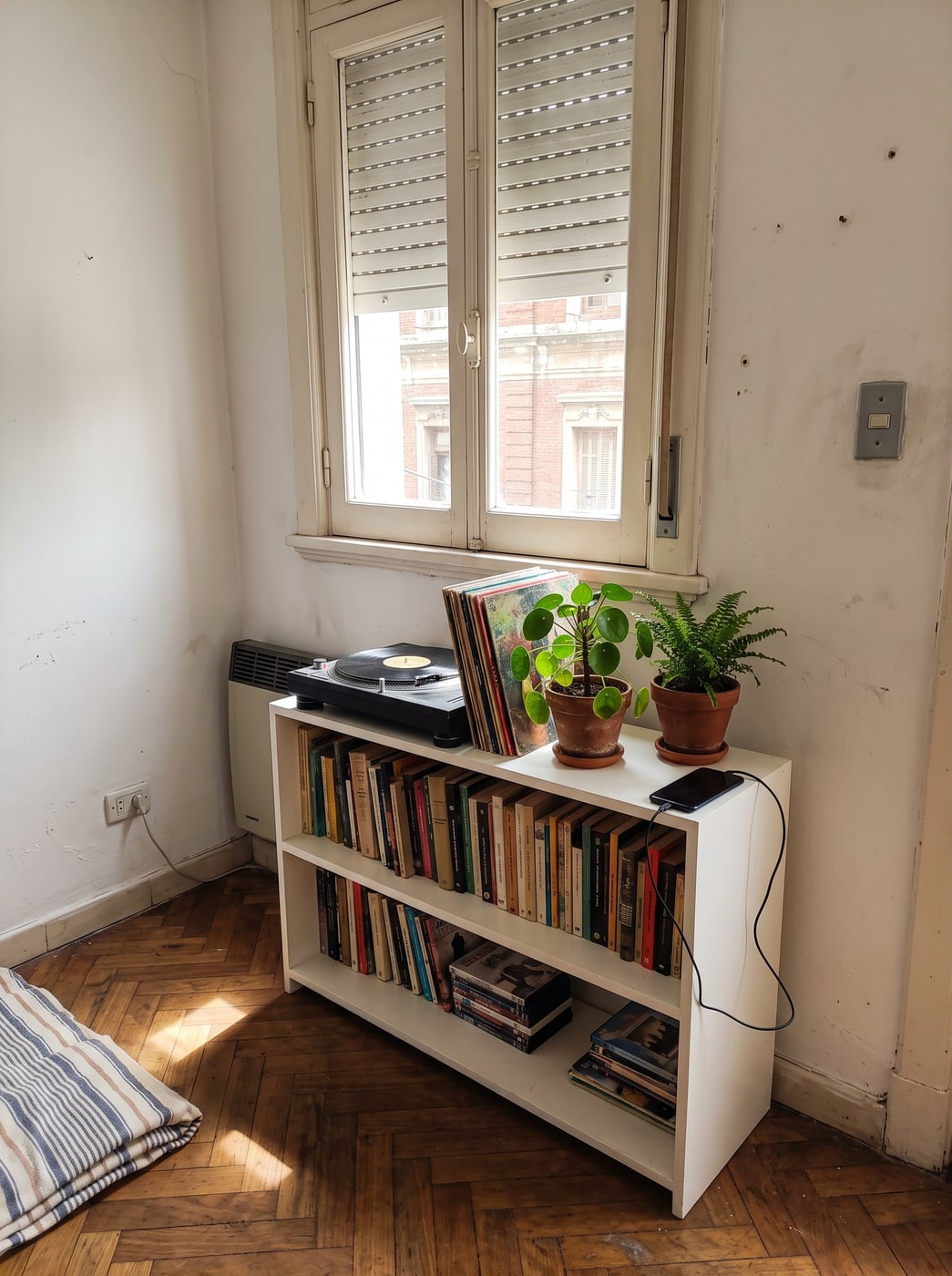 Biblioteca baja laqueada en blanco debajo de una ventana, con tocadiscos, discos de vinilo y plantas encima.