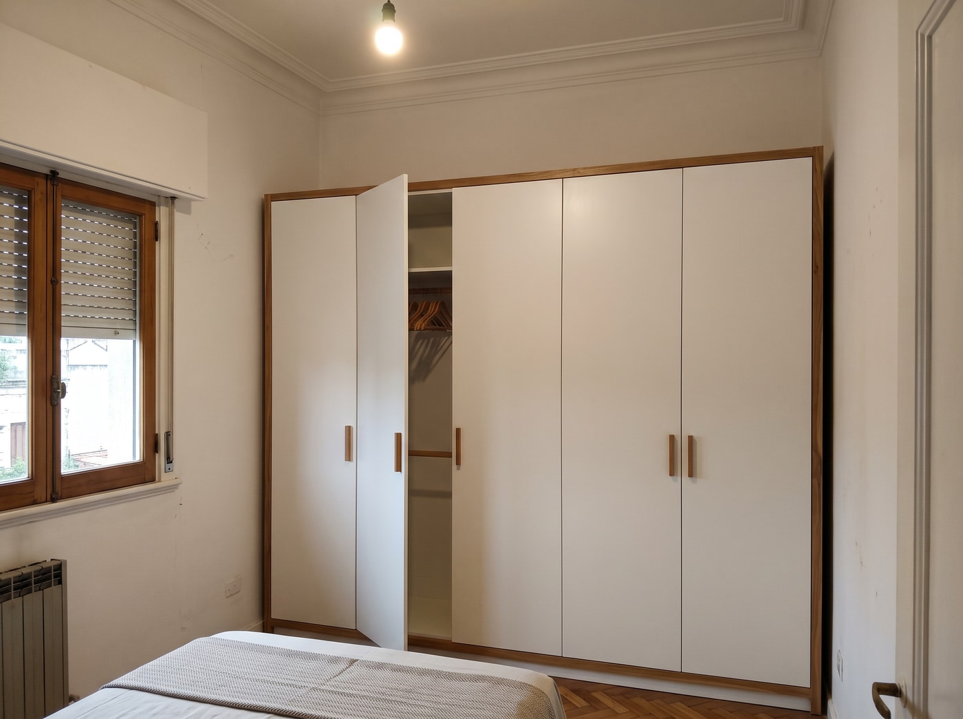 Placard de piso a techo laqueado en blanco con cinco puertas batientes, una entreabierta, en un dormitorio de techo alto con piso de parquet.