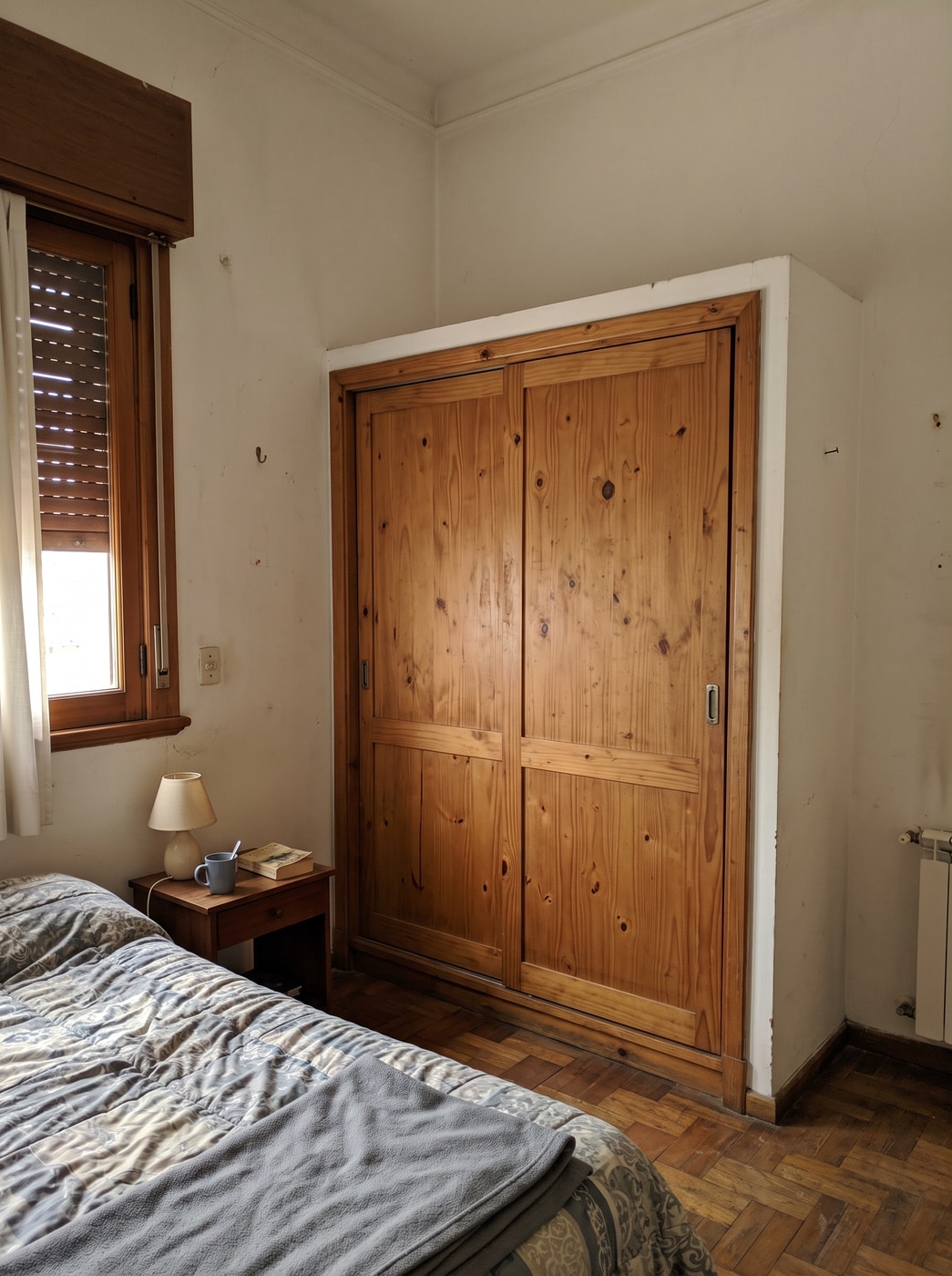 Placard de pino macizo con dos puertas corredizas en un dormitorio chico, con la cama y la mesa de luz al lado.