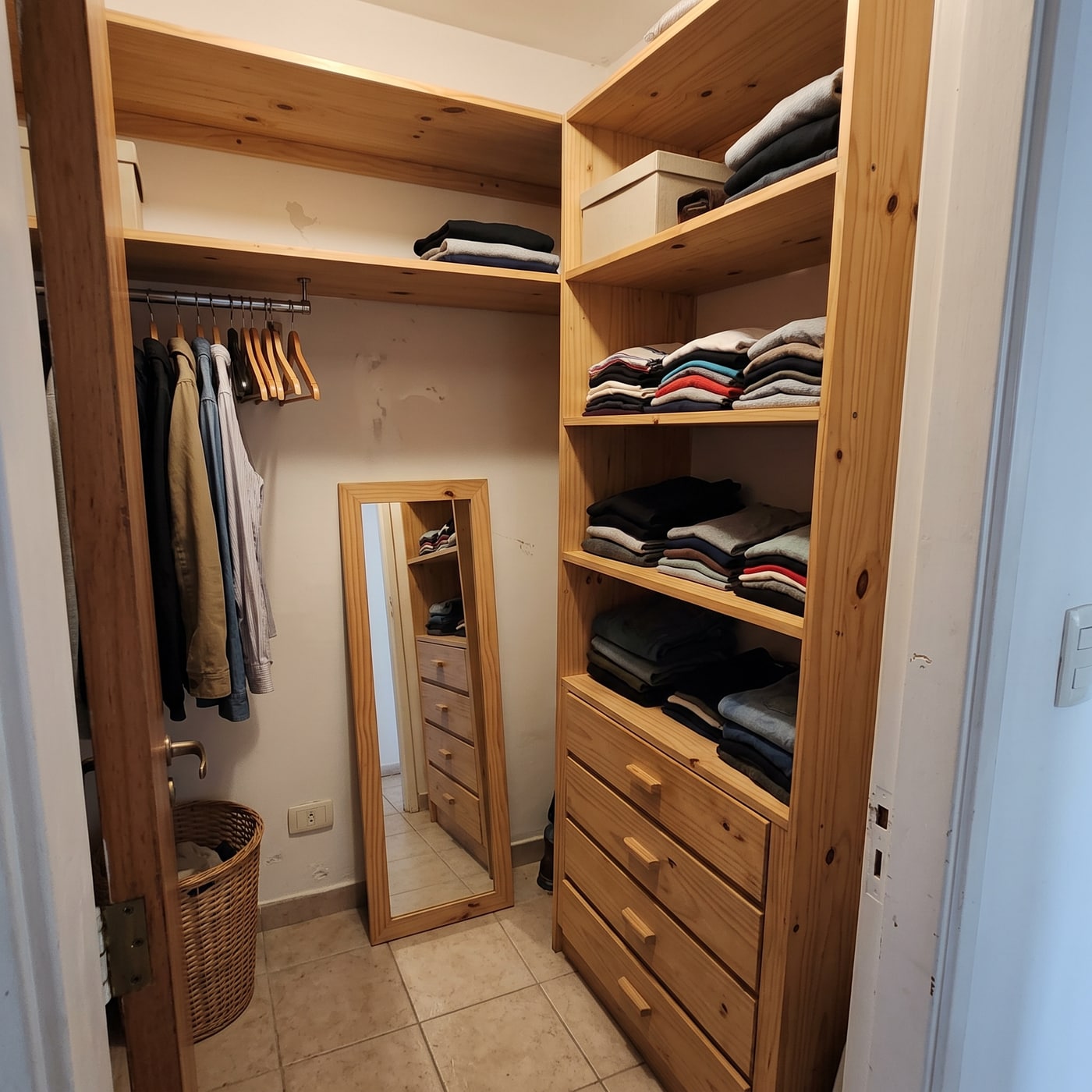 Vestidor chico en L de pino natural con estantes abiertos, cajonera, barral y espejo de pie apoyado en la pared.