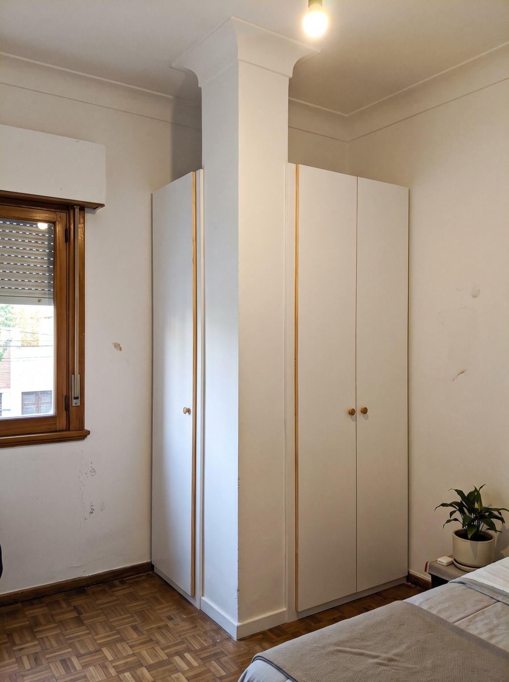 Placard laqueado blanco de piso a techo construido a ambos lados de una columna en un dormitorio de apartamento antiguo con parquet.